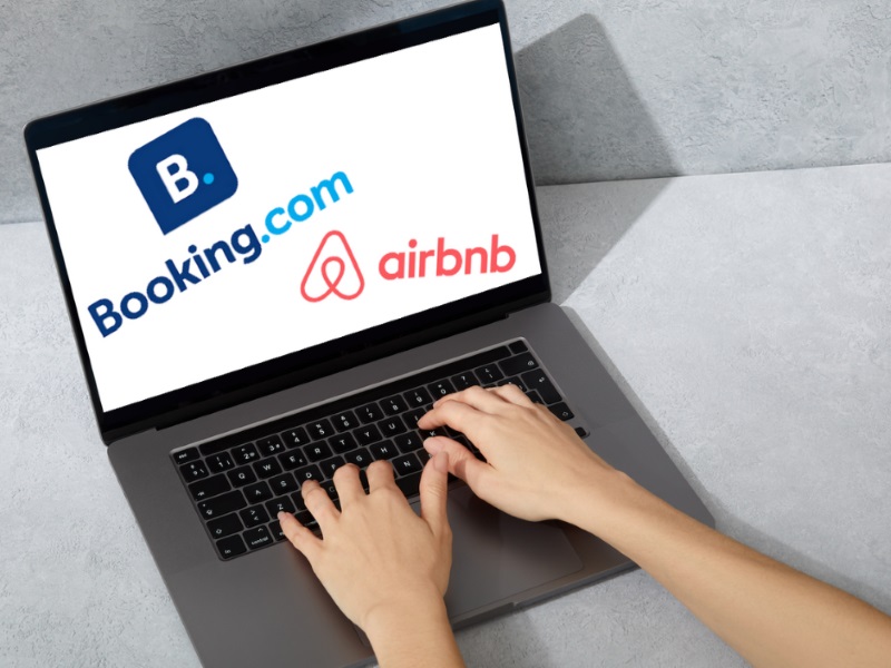 Roke tipkajo po prenosniku, na katerem piše Booking.com in Airbnb.