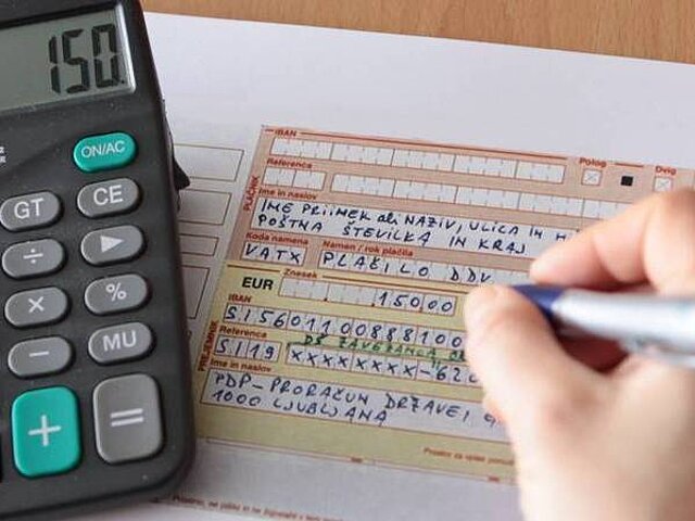 Ženska ročno izpolnjuje U P N nalog. Poleg je na mizi tudi kalkulator.
